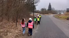 elever med färgglada reflexvästar går tillsammans två och två vid sidan av en väg.