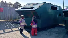 Två barn står framför en grön sopcontainer för att återvinna skräp.