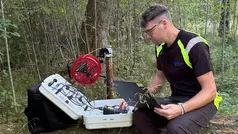Christoffer Österling sitter på en stubbe med en laptop i kbät och en verktygslåda han kollar av värden på.