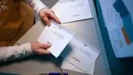 Person håller i ett valkuvert bakom en röstskärm.
