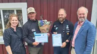 Fyra personer står bredvid varandra, de i mitten håller upp diplom och blommor.