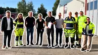 En grupp personer står utomhus, en person håller i en inramad diplom. Det är soligt och fint väder. se ser glada ut.