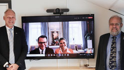kommunchef Magnus Nilsson och kommunstyrelsensordförande Stefan Carlsson står på varsin sida om en TV skräm på vilken en videomötesruta syns med kronprinsessparet