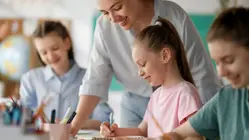 En lärare står och hjälper elever vid deras bord.