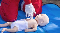 Räddningspersonal med plasthandskar på visar HLR på baby docka.